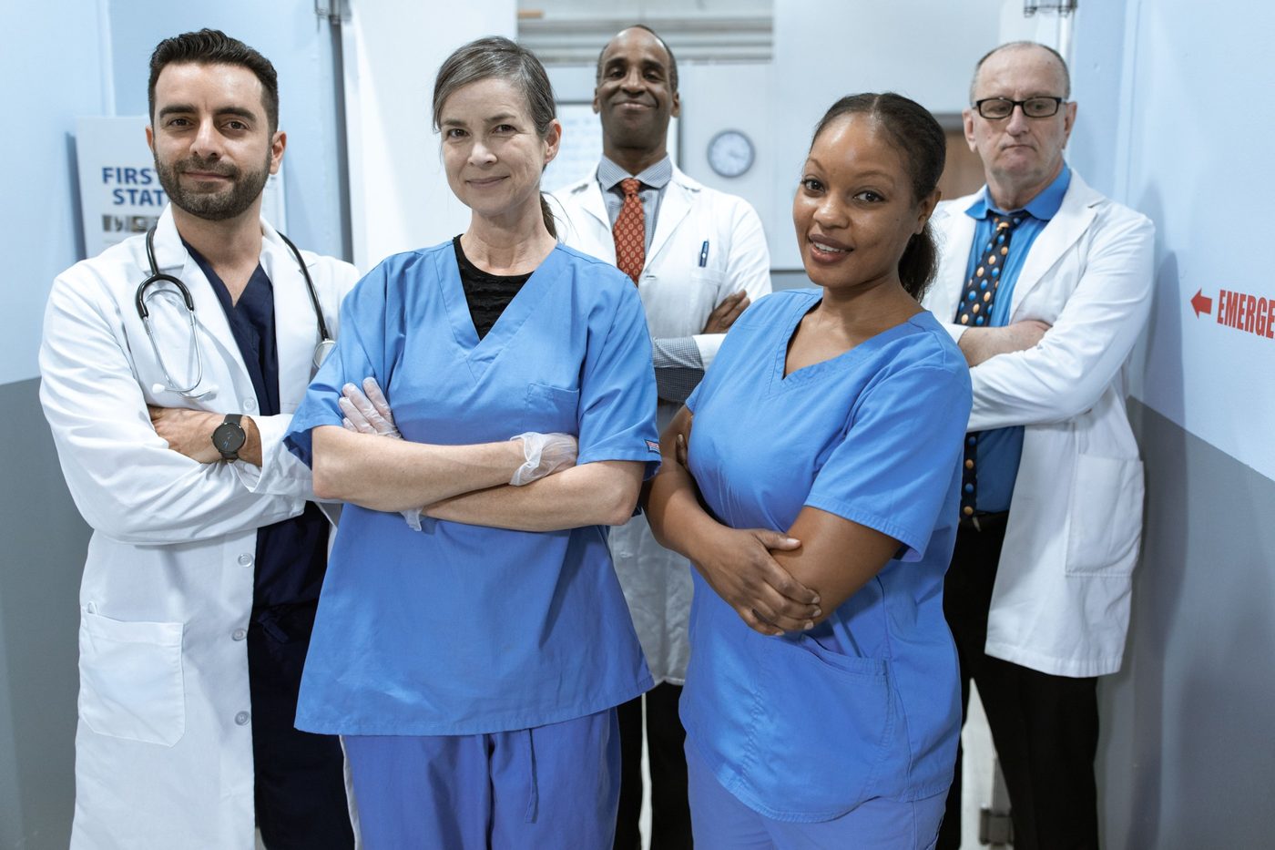 Doctors in white coats and nurses in blue scrubs standing together in a hospital hallway
